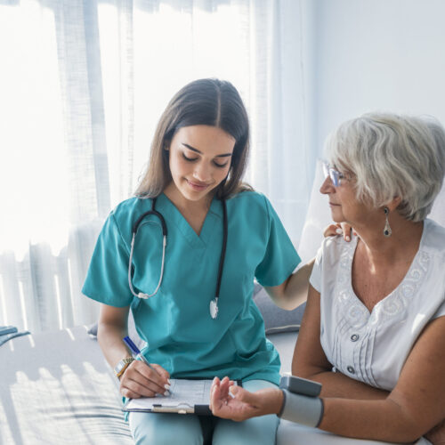 Nurse measuring blood pressure of senior woman at home Nurse doing blood pressure monitoring for senior woman at home. Close up photo of blood pressure measurement. Nurse measuring blood pressure of senior woman at home. Smiling to each other.